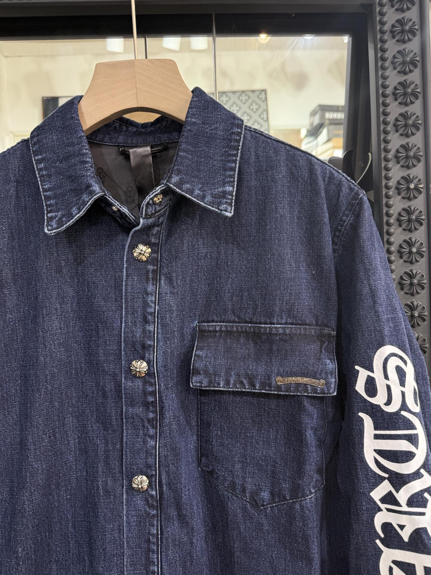 Chrome Hearts logo on the arm with Sanskrit lettering; large silver scroll and cross design on the chest; blue denim jacket. Sizes: S, M, L.