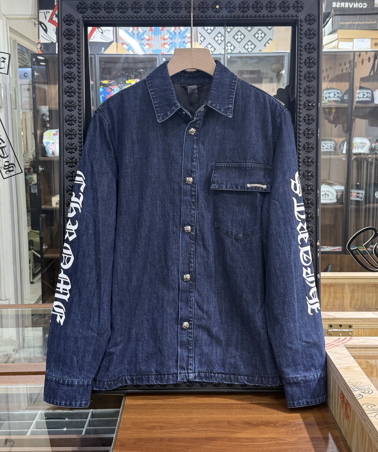 Chrome Hearts logo on the arm with Sanskrit lettering; large silver scroll and cross design on the chest; blue denim jacket. Sizes: S, M, L.